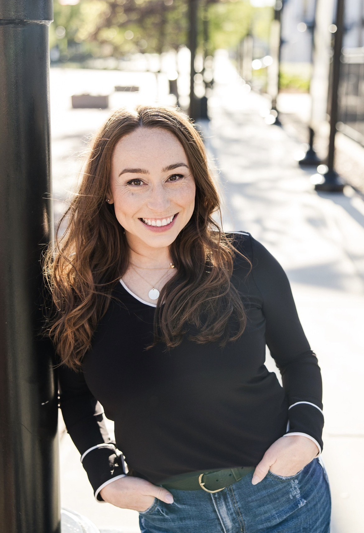 Molly Schunicht leaning against light pole smiling with hands in pockets
